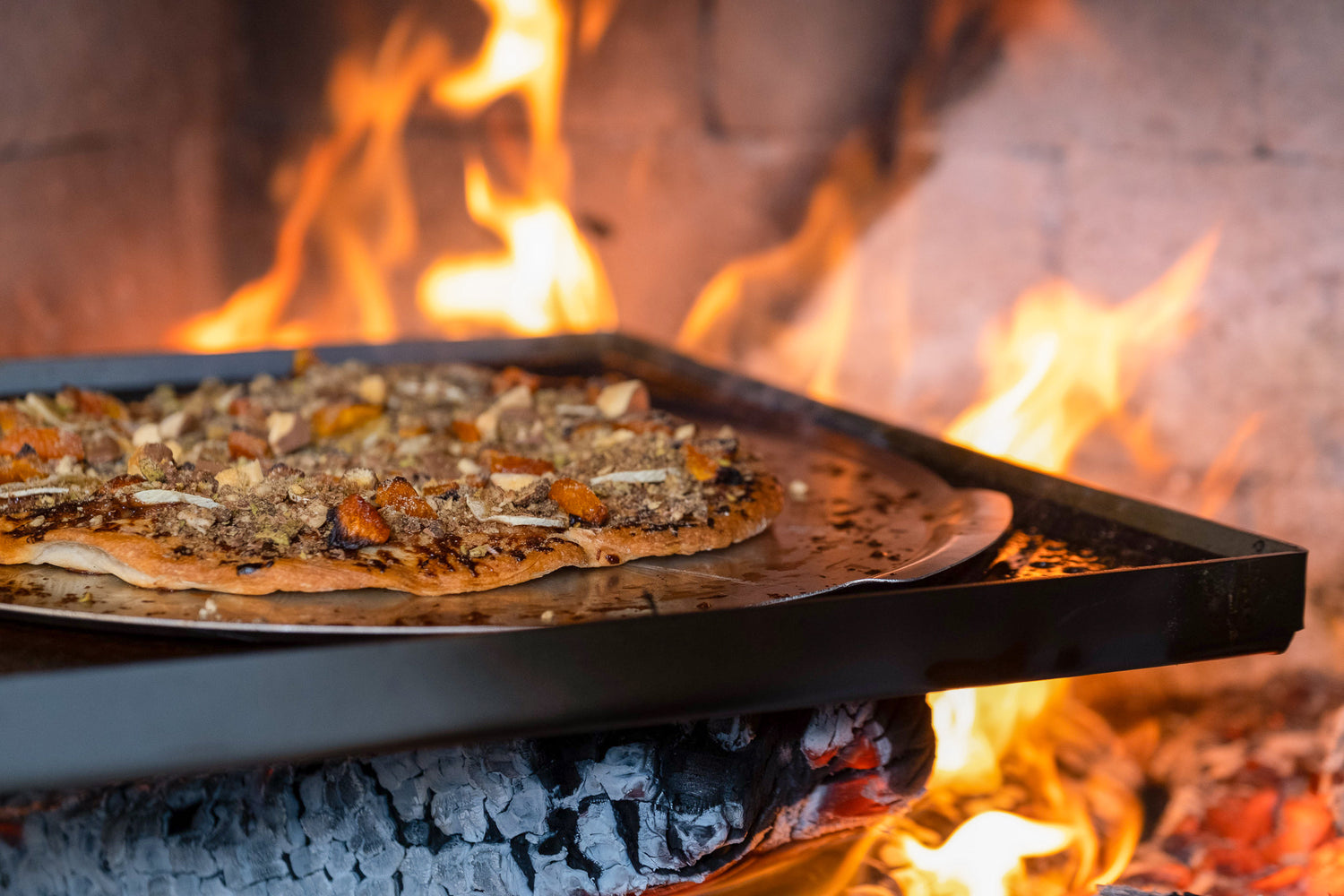 A sweet pizza sits in a pizza oven with roaring flames in the background. 